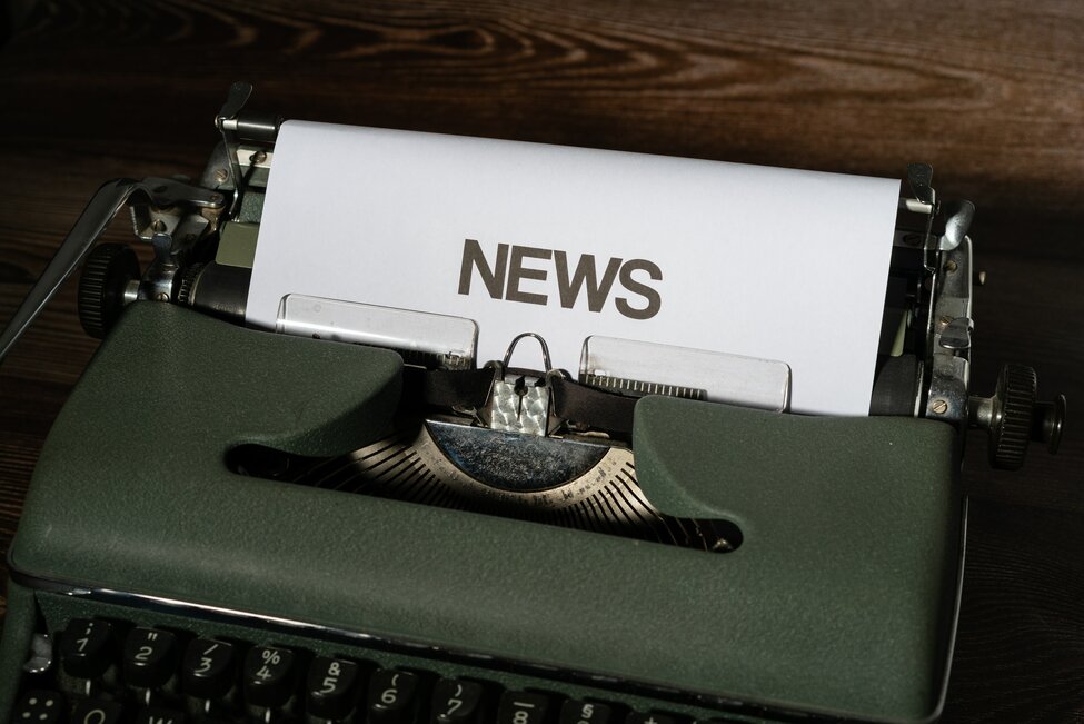 top of old green typewriter with a paper in i and the word "news" printed on it