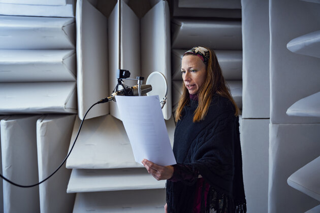 kvinna som står och läser från ett papper med en mikrofon hängande från taket. På väggarna finns det ljudisolerande material.