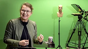 [Translate to English:]  Marianne Gullberg i LARM-­studion med en greenscreen bakom sig, som bland annat ger studenter möjlighet att öva på att göra en väderpresentation. Foto: Kennet Ruona 