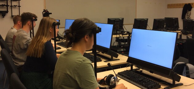 [Translate to Svenska:] four persons sitting with heads in chin rests in fron of computers, singing