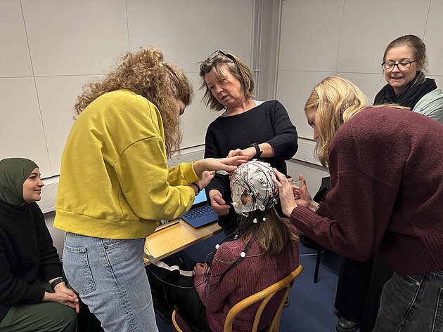 several persons fitting a eeg-cap on a person sitting down in fron of a mirror