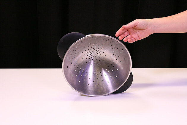 colander balancing on surface with a hand right next to it