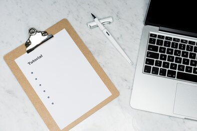 a clipboard with a paper and the word tutorial and bulletpoints on it, a pen, and a piece of a laptop