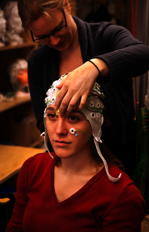 one person is putting on a EEG cap and electrodes on another person