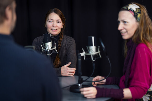 three persons are sitting talking around a table with microphones