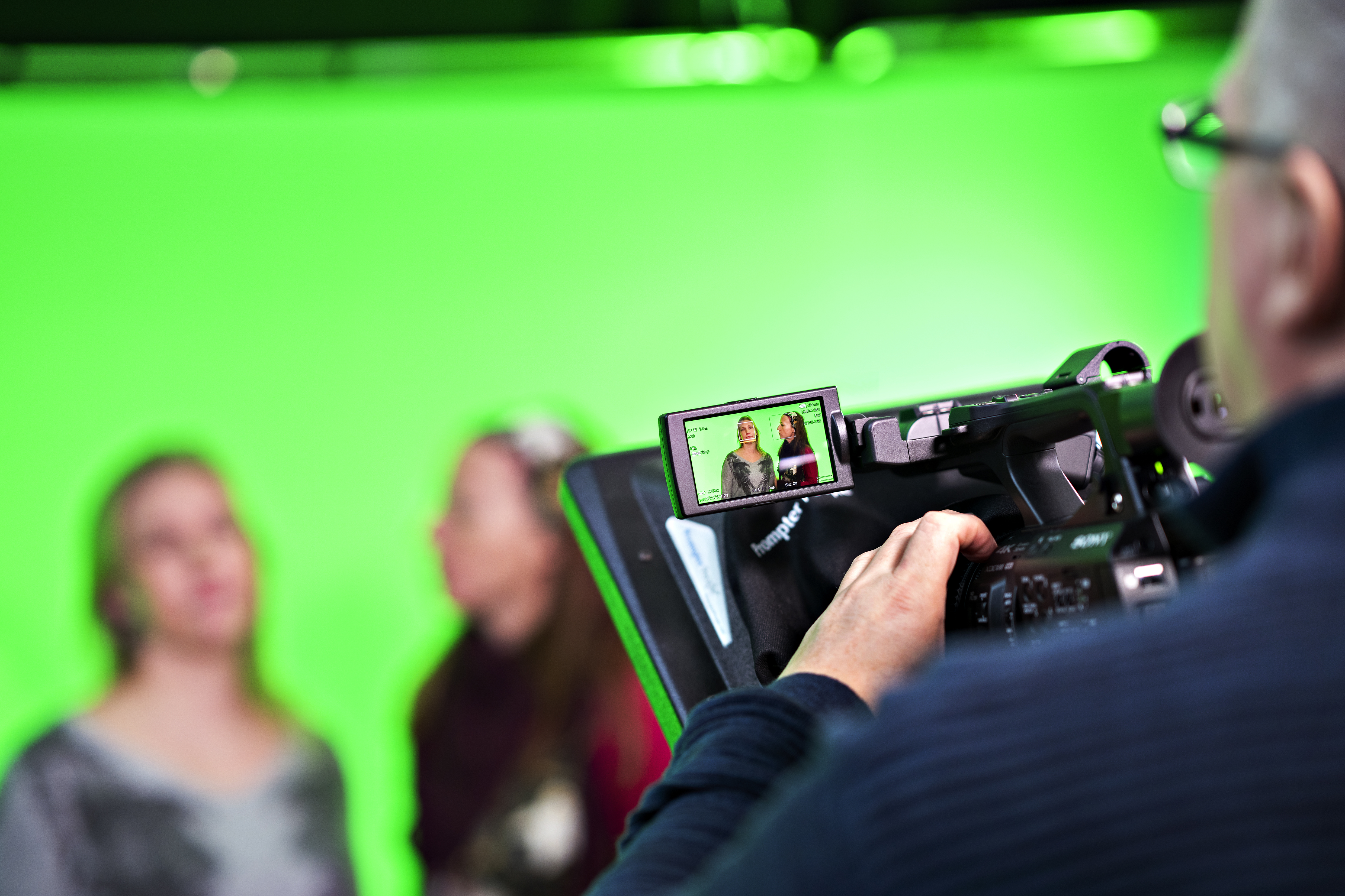 a green scren with to blurry people in fron a a close up of a camera screen with the people in focus on it
